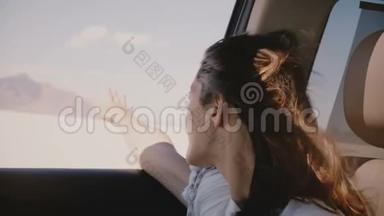 在盐湖沙漠，一个快乐的年轻女人，她的头发飞扬，手从窗外开着车，快速地移动着。